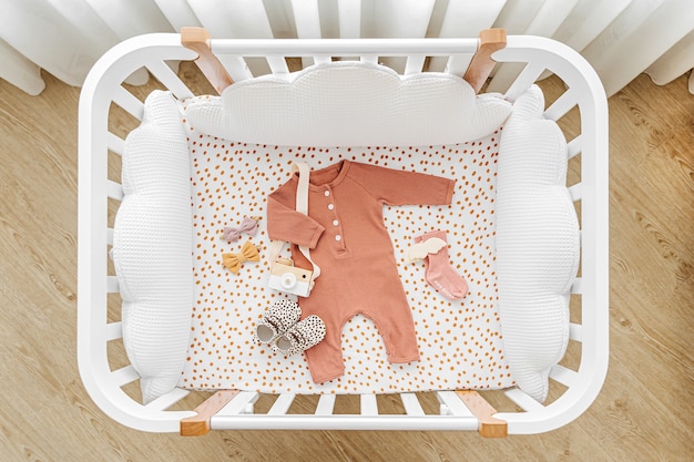 Cuna de madera blanca con almohadas en forma de nubes en la habitación del bebé. Ropa y complementos de recién nacido en cuna. Vista superior de la cama del niño