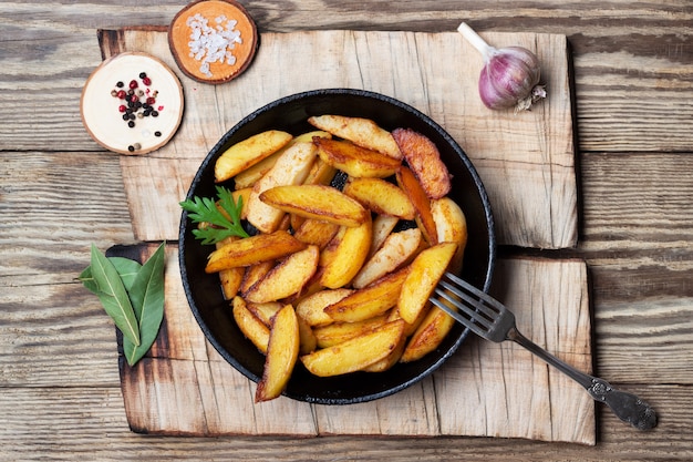 Cuñas de papas fritas en una sartén sobre la mesa de madera. Vista superior.