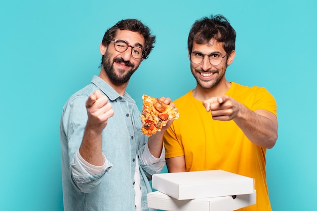 Cuople de dos amigos hispanos apuntando o mostrando y sosteniendo pizzas para llevar