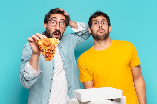 Cuople de dos amigos hispanos expresión asustada y sosteniendo pizzas para llevar