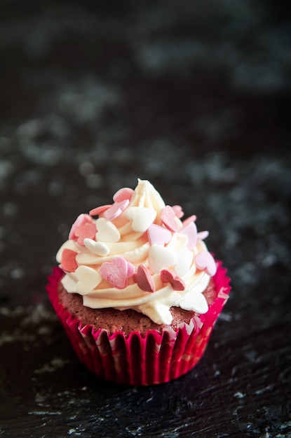 Cupcake de celebración para el día de San Valentín en mesa de madera negra con corazones.