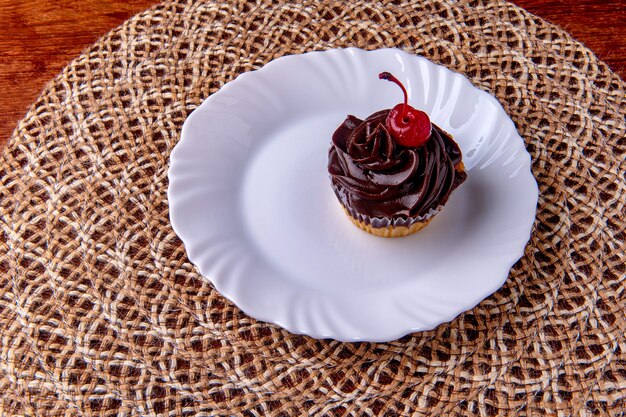 Foto cupcake de chocolate con cereza en un plato sobre la mesa de madera.