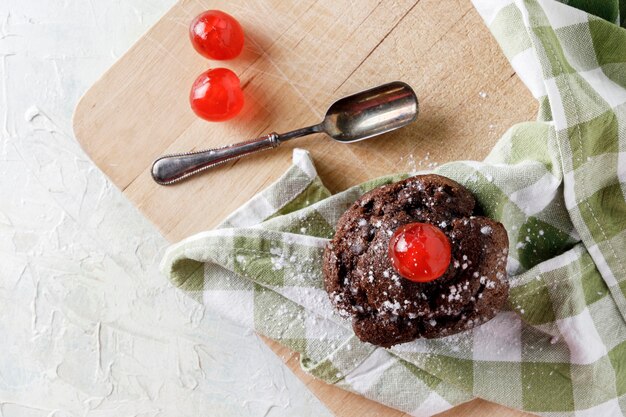 Cupcake de chocolate con glaseado en servilleta sobre tabla de madera y cuchara vieja