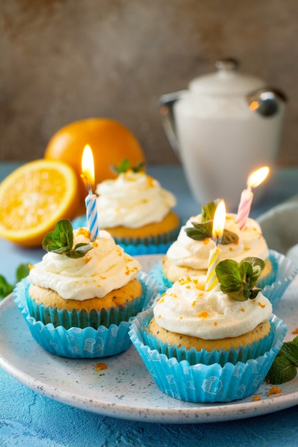 Cupcake colorido de laranja com vela de aniversário em um fundo azul de pedra ou ardósia