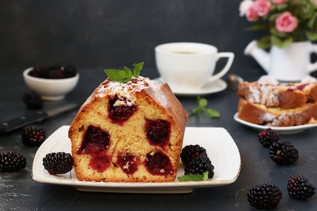 Cupcake com amoras está localizado em um prato branco em uma superfície escura, seção do bolo em primeiro plano