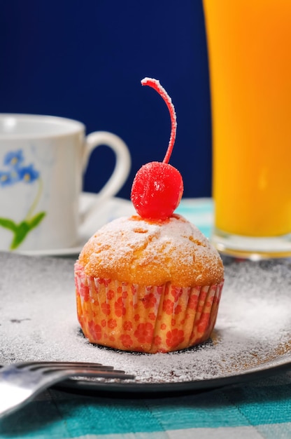 cupcake com cereja e uma xícara de chá com um copo de suco de laranja