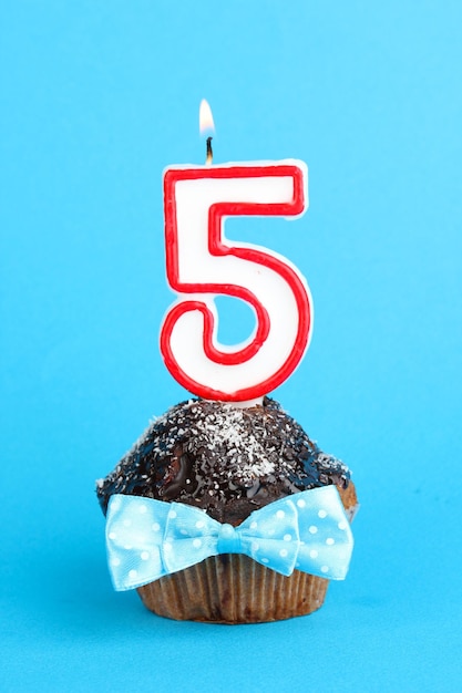 Cupcake de cumpleaños con glaseado de chocolate sobre fondo azul.