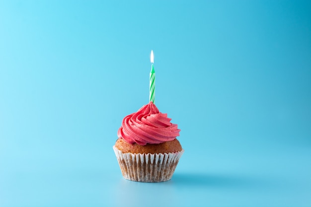 Cupcake de cumpleaños rosa con vela verde sobre fondo azul.