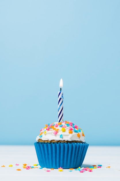 Cupcake de cumpleaños con velas sobre fondo azul.