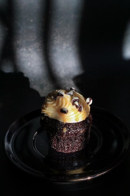 Foto cupcake de chocolate com creme de manteiga na cozinha do restaurante com fundo escuro sob a luz do sol