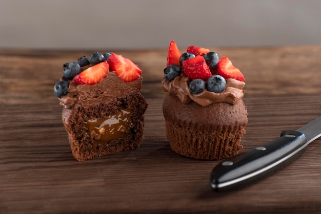 Cupcake de chocolate cortado é decorado com creme de manteiga de chocolate e frutas Sobremesa e faca em tábua de madeira áspera