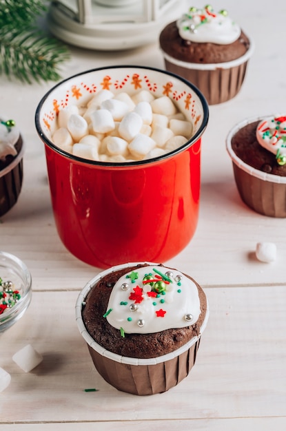 Cupcake de chocolate de Natal com cobertura de açúcar colorido e xícara de chocolate com marshmallow