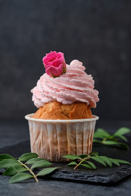 Cupcake decorado com rosas. Sobremesa em um prato de ardósia preta. Bolos em um fundo escuro.