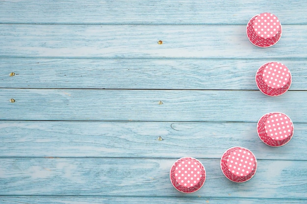 Cupcake-Förmchen mit rosa Tupfen auf blauem Holzboden. Materialien oder Küchengeräte für die Bäckerei.