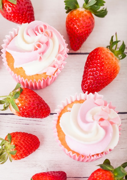 Cupcake-Muffin mit Erdbeer-Sahne-Dessert auf Holztisch mit frischen Erdbeeren