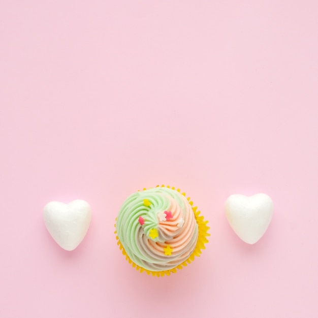 Cupcake pastel y corazones blancos sobre fondo rosa