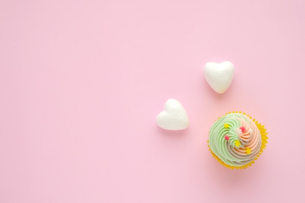 Cupcake pastel y corazones blancos sobre fondo rosa