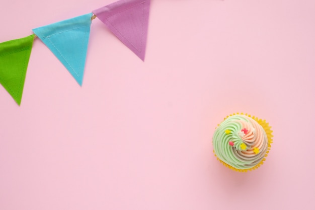 Cupcake pastel e bandeira colorida do partido no fundo cor-de-rosa