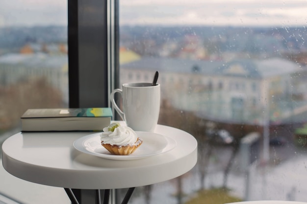 Cupcake con taza en la mesa blanca junto a la ventana en el café