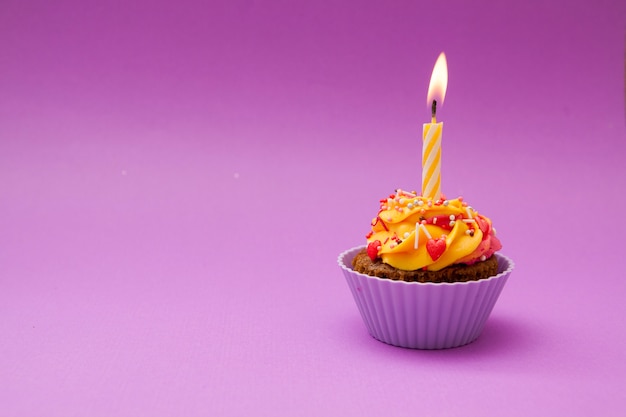 Cupcake con una vela y corazones sobre una superficie lila. . Concepto de día de San Valentín