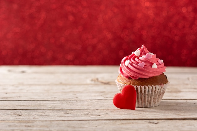 Cupcake verziert mit Zuckerherzen zum Valentinstag auf Holztisch und rotem Hintergrund