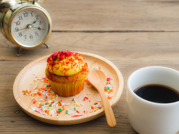 Los cupcakes amarillos ponen en la placa de madera al lado del reloj de la vendimia y el café con leche