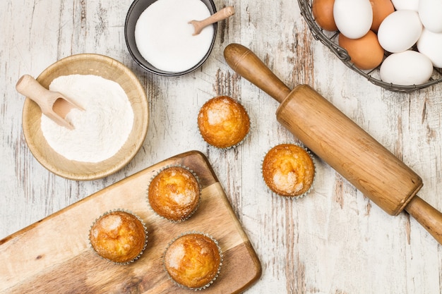 Cupcakes auf einem hölzernen Küchentisch mit Zuckereiern und einem Nudelholz