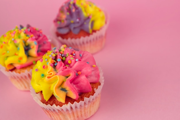 Cupcakes caseiros com creme multi-colorido em um espaço de cópia de fundo rosa. Creme amarelo e rosa.