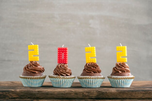 Cupcakes de chocolate con coloridas velas 2022 en mesa de madera. Concepto de vacaciones de año nuevo. Fondo gris.