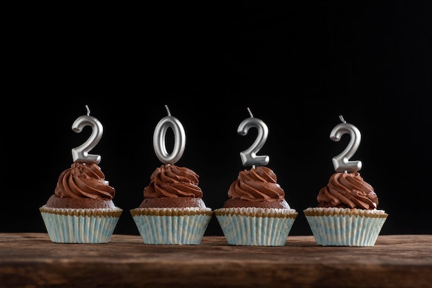 Cupcakes de chocolate con glaseado de crema de mantequilla con velas de plata 2022 sobre mesa de madera sobre fondo negro.