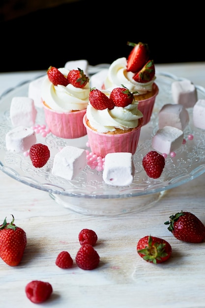 Cupcakes com chantilly e creme doce decorado com morangos Em um suporte de vidro com marshmallows