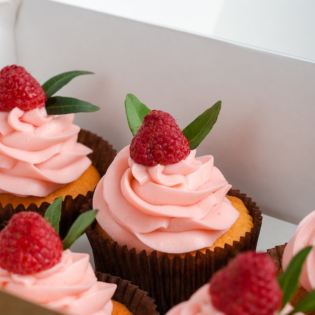 Cupcakes com creme de framboesa, decorado com framboesas em cima no embrulho.