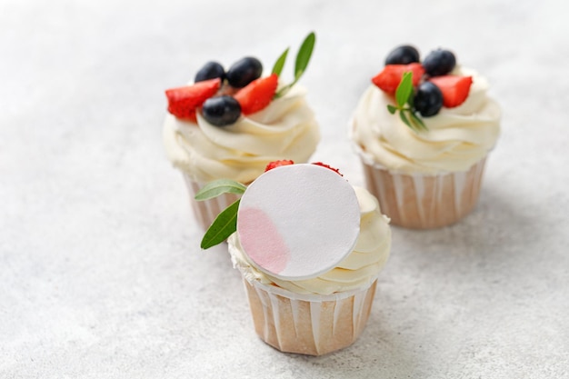 Cupcakes com folhas de creme de baunilha de frutas frescas em fundo cinza sobremesa simulada para foto