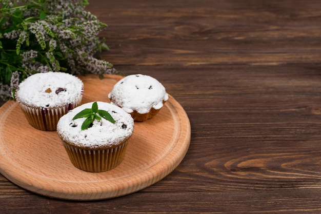 Cupcakes com groselhas pretas em um fundo de flores e folhas de hortelã em uma placa redonda em um fundo de madeira