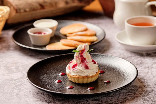 Cupcakes con crema de vainilla blanca batida con panqueques y mermelada de bayas, una taza de café negro americano para el desayuno