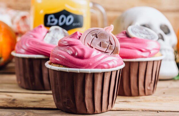 Foto cupcakes de abóbora de halloween felizes decorados com creme rosa e chocolate colorido em fundo de madeira rústica foco seletivo