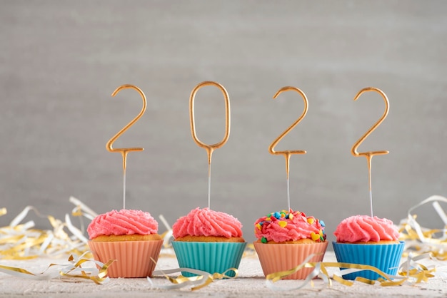 Cupcakes de ano novo e espumantes dourados números 2022. Muffins de Natal com cobertura de creme de manteiga rosa. Plano de fundo cinza.