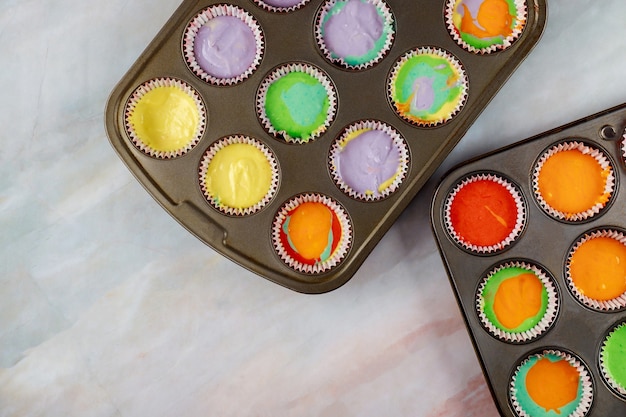 Cupcakes de arco-íris crus em uma bandeja de dois fornos. Vista do topo.