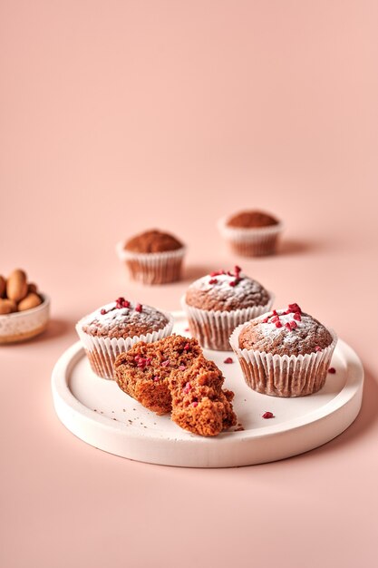 Cupcakes de chocolate caseiros em formas de papel manteiga e pedaços deles na placa de luz em pó rosa