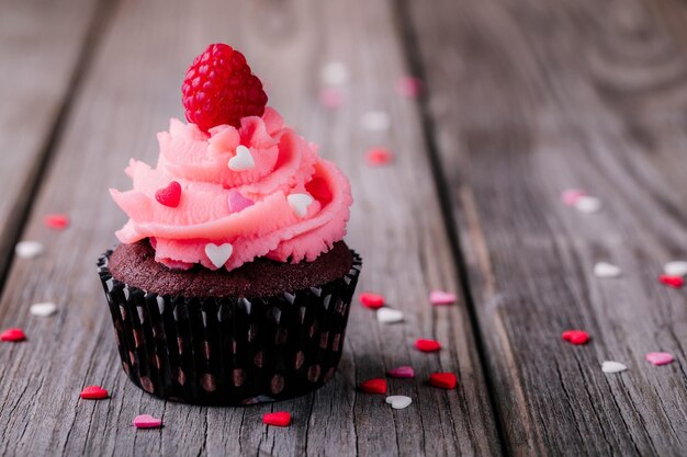 Cupcakes de chocolate com corações de açúcar creme rosa e framboesas frescas para o dia dos namorados