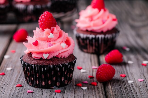 Cupcakes de chocolate com corações de açúcar creme rosa e framboesas frescas para o dia dos namorados