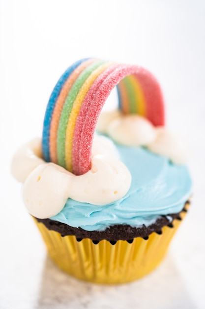 Cupcakes de chocolate decorados com cobertura de creme de manteiga azul e arco-íris para festa de aniversário com tema de unicórnio.