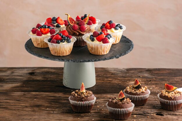 Cupcakes de chocolate e baunilha com mistura de bagas no suporte na mesa de madeira. Muffin com frutas.