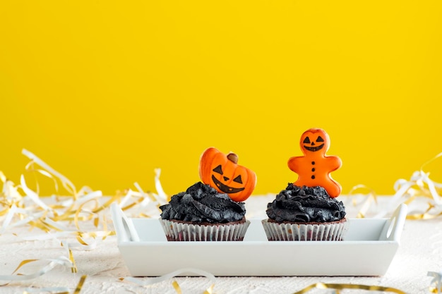 Cupcakes de férias com creme preto para comemorar muffins de halloween decorados com pão de gengibre em fundo amarelo