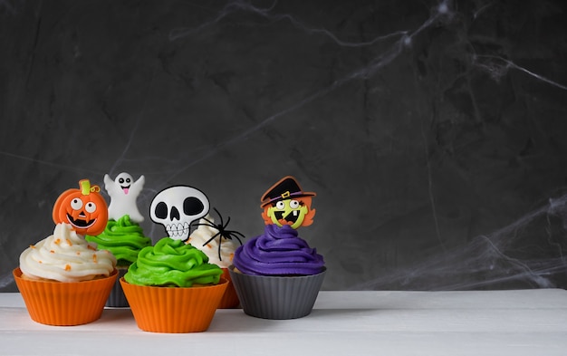 Cupcakes de halloween assustadores brilhantes em um fundo escuro com teias de aranha. creme colorido e decoração.