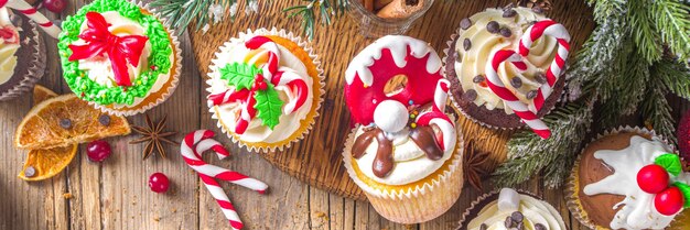 Cupcakes de Natal engraçados. Cupcakes doces caseiros com cobertura de açúcar em forma de decoração de Natal e símbolos, em fundo de madeira com decoração de Natal