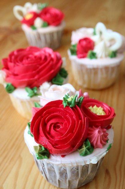 Cupcakes decorados con crema batida en forma de flor roja sobre mesa de madera con enfoque selectivo