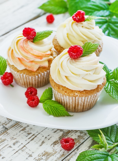 Cupcakes delicados de baunilha com creme e framboesas em uma mesa de madeira branca