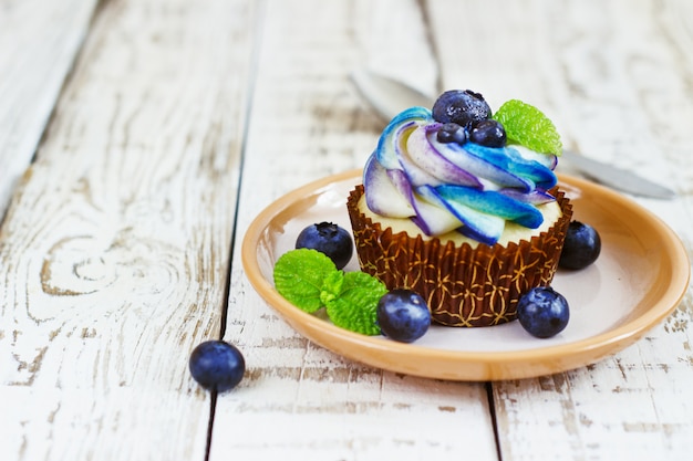 Cupcakes delicados de baunilha com creme e frutas em um branco de madeira