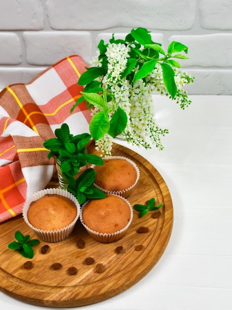 Cupcakes em uma placa de madeira com passas e um buquê de flores brancas Três cupcakes em uma lousa com uma toalha de mesa e um buquê de flores em uma mesa de madeira branca
